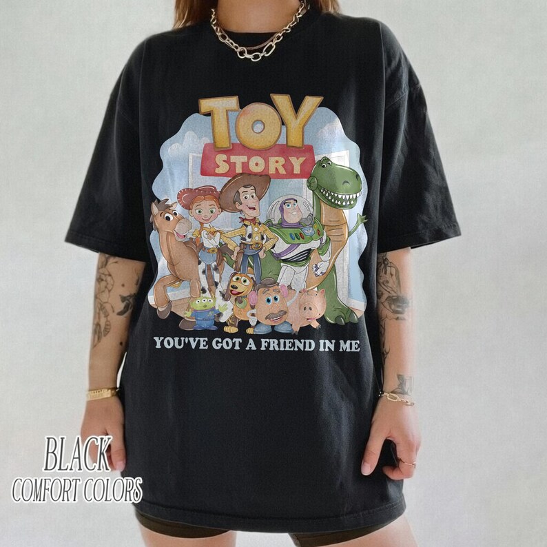K&ouml;nnte beinhalten: Schwarzes T-Shirt mit einer farbenfrohen Grafik von Charakteren aus dem Film "Toy Story". Das Design enth&auml;lt den Filmtitel und den Satz "You've Got a Friend in Me". Auf dem Shirt steht auch "Black Comfort Colors".