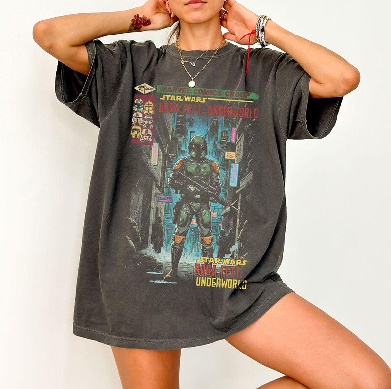 Puede incluir: Camiseta gris oscuro con un dise&ntilde;o de Boba Fett de Star Wars, en un callej&oacute;n de la ciudad. La camiseta incluye el texto "Marvel Comics Group Star Wars Boba Fett Underworld" en verde y rojo. El dise&ntilde;o es de inspiraci&oacute;n vintage.