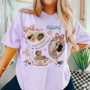 Puede incluir: Una camiseta de color lila claro con la palabra "Moana" e ilustraciones de dibujos animados. El dise&ntilde;o incluye im&aacute;genes de Moana, un cerdo, un gallo y otros elementos decorativos. La camiseta tiene mangas cortas.