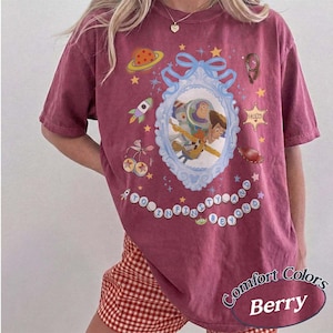 Peut inclure: Un t-shirt &agrave; manches courtes couleur baie avec un cadre orn&eacute; bleu clair central contenant Buzz l'&Eacute;clair et Woody. Les graphismes incluent une plan&egrave;te, une fus&eacute;e, une &eacute;toile de sh&eacute;rif et le texte TO INFINITY AND BEYOND en perles circulaires.