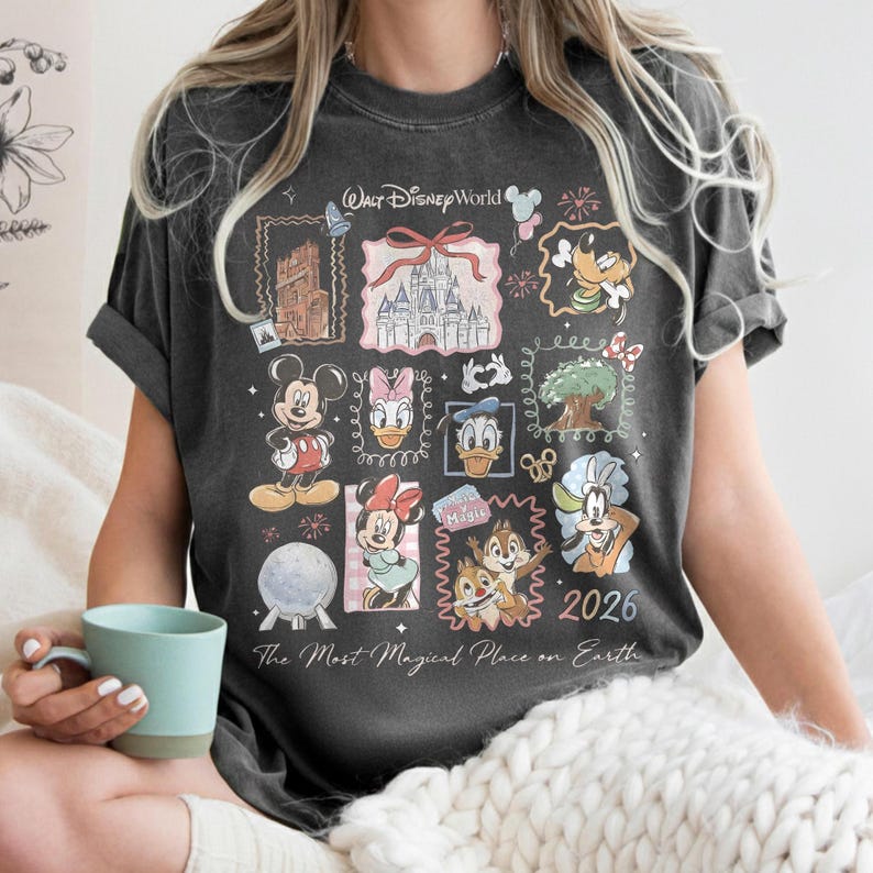 May include: Dark gray t-shirt featuring a collage of Disney characters and landmarks, including Mickey Mouse, Donald Duck, and Cinderella's castle. The shirt has the text "Walt Disney World" and "2026" with the phrase "The Most Magical Place on Earth".
