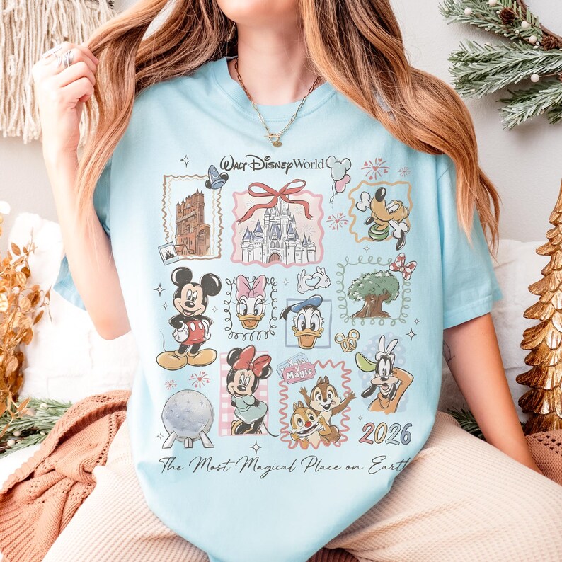 May include: Light blue t-shirt featuring a collage of Disney characters and landmarks. The design includes Mickey Mouse, Minnie Mouse, Donald Duck, and Goofy, along with Cinderella's castle and the text "Walt Disney World" and "2026". The shirt also has the text "The Most Magical Place on Earth."