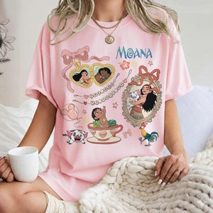Puede incluir: Camiseta rosa con ilustraciones de personajes y elementos de la pel&iacute;cula de animaci&oacute;n "Moana". El dise&ntilde;o incluye la palabra "Moana", retratos de personajes y otros gr&aacute;ficos tem&aacute;ticos. La camiseta es de manga corta.