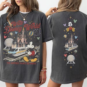 Peut inclure: Un t-shirt gris anthracite avec une impression graphique de Walt Disney World, incluant le ch&acirc;teau de Cendrillon, un monorail et Mickey Mouse. Le texte indique Walt Disney World et The Happiest Place on Earth, avec des feux d'artifice.