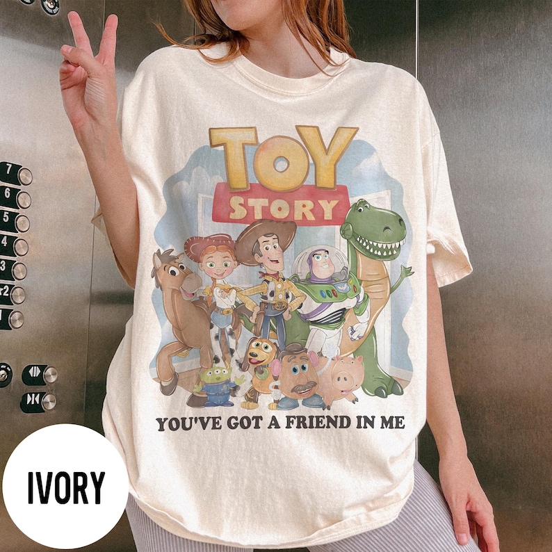 K&ouml;nnte beinhalten: Elfenbeinfarbenes T-Shirt mit dem Schriftzug "TOY STORY" und einer Grafik von Figuren aus dem Animationsfilm. Der Satz "YOU'VE GOT A FRIEND IN ME" ist darunter gedruckt. Das Shirt hat eine lockere Passform.