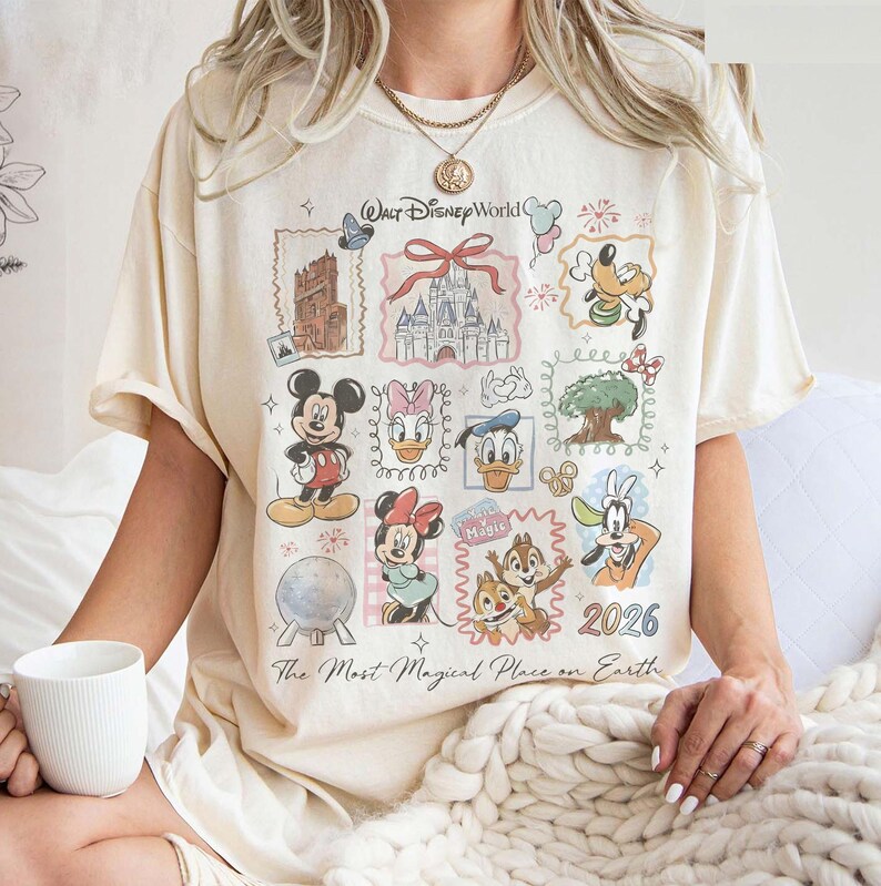 May include: Cream-colored t-shirt featuring a colorful graphic of Disney characters and landmarks. The design includes Mickey Mouse, Minnie Mouse, Donald Duck, and other characters, with the text "Walt Disney World" and "2026". The shirt also has the text "The Most Magical Place on Earth."