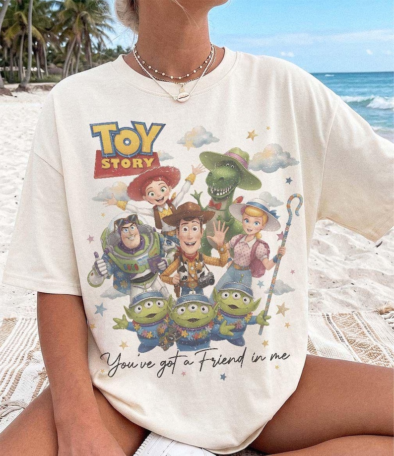 Puede incluir: Una camiseta de color crema con un estampado gr&aacute;fico colorido de los personajes de Toy Story, incluyendo a Woody, Buzz Lightyear, Jessie, Rex, Bo Peep y tres alien&iacute;genas. El texto "TOY STORY" y "You've got a Friend in me" est&aacute; impreso al frente.