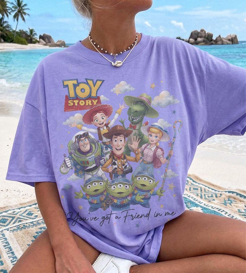 Puede incluir: Una camiseta de color morado claro con un estampado gr&aacute;fico de los personajes de Toy Story, incluyendo a Woody, Buzz Lightyear, Jessie, Bo Peep, Rex y los Aliens. El texto Toy Story aparece arriba y la frase You've got a Friend in me debajo.
