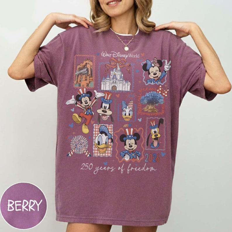 Może przedstawiać: Jagodowa koszulka z kr&oacute;tkim rękawem z nadrukiem graficznym przedstawiającym postacie Disneya w patriotycznych strojach, zamek Walt Disney World oraz napis 250 years of freedom 2026. Wz&oacute;r zawiera Myszkę Miki, Minnie, Kaczora Donalda i Goofy'ego.