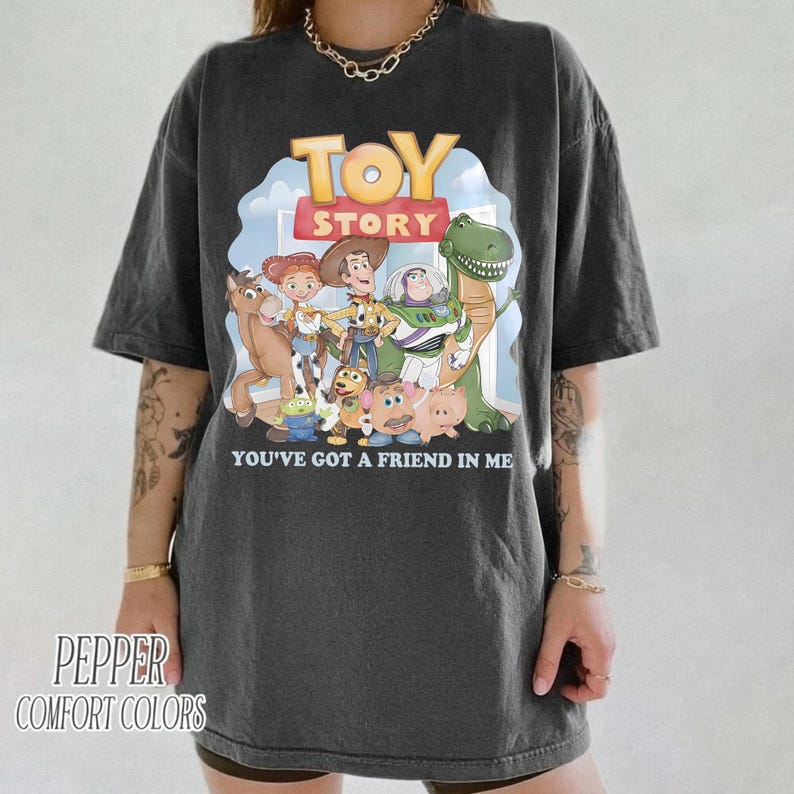 K&ouml;nnte beinhalten: Dunkelgraues T-Shirt mit dem Toy Story-Logo und -Charakteren. Die Grafik zeigt Woody, Buzz Lightyear und Rex mit dem Text "YOU'VE GOT A FRIEND IN ME". Das Shirt ist von Pepper Comfort Colors.