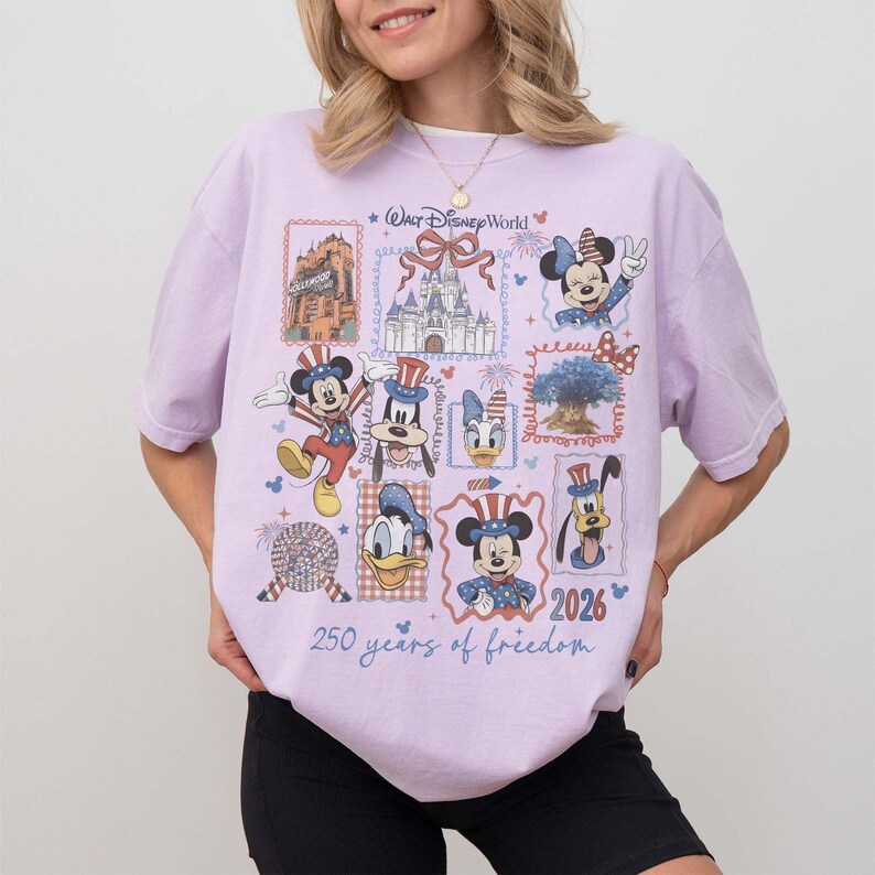 Może przedstawiać: Jasnofioletowy t-shirt z nadrukiem graficznym przedstawiającym zabytki i postacie z Walt Disney World w patriotycznych strojach. Projekt zawiera tekst Walt Disney World, 2026 oraz 250 years of freedom, otoczony r&oacute;żnymi ilustracjami w ramkach.