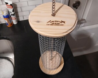 May include: A handcrafted wooden bird feeder with a wire mesh cylinder and a wooden top and bottom. The top is attached to a chain for hanging. The text "HAND CRAFTED BY OAK DEN WOODWORK" is visible on the top.