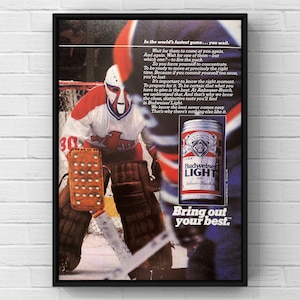 May include: Framed vintage advertisement for Budweiser Light beer. The image features a hockey goalie in a red, white, and blue uniform. The ad includes text about the beer and the phrase "Bring out your best."
