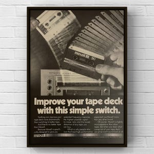 May include: Black and white advertisement for Maxell audio cassettes. The image shows a stack of cassettes, a hand holding a cassette labeled "Maxell 90", and a stereo receiver. The text reads "Improve your tape deck with this simple switch."