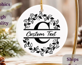 May include: A white ceramic ornament with a gold hanging cord. The ornament features a black floral wreath design around a large letter and the words "Custom Text". The ornament is displayed on a gold stand.