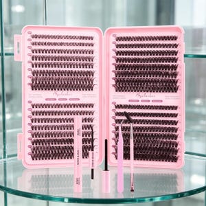 Könnte beinhalten: Ein rosa Wimpernverlängerungs-Set mit einer Vielzahl von Einzelwimpern, Werkzeugen und Klebstoff. Das Set enthält eine Hülle mit mehreren Wimpernreihen, eine Mascarabürste, eine Pinzette und eine Tube Wimpernkleber und Versiegelung.