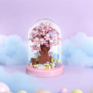 May include: A miniature pink cherry blossom tree inside a glass dome. The tree has pink and white flowers, with a brown trunk and branches. A light purple butterfly and blue flowers are also inside the dome, which sits on a pink base.
