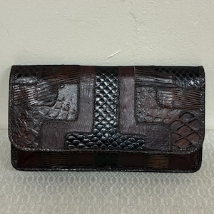 May include: A rectangular clutch with a patchwork design. The clutch features a mix of textures and patterns in shades of brown, black, and burgundy. The flap closure is visible, and the overall aesthetic is vintage.