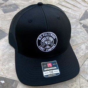 May include: Black trucker hat with a white embroidered logo that says "Old Hollywood Light Company" and a black and red label that says "Richardson 112 Original Trucker Adjustable".