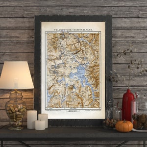 May include: A vintage map of Yellowstone National Park, framed in black, with a brown wooden background. The map shows the park's features, including rivers, lakes, and mountains.