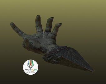 Könnte beinhalten: Eine dunkelgraue, texturierte Skulptur einer abgetrennten Hand mit ausgestreckter Handfläche und Fingern, die eine spitze, dreieckige Basis mit vertikalen Streifen aufweist. Ein kreisförmiges Logo mit dem Text MULTICOLOR PRINT READY ist unten links sichtbar.