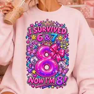 Pode incluir: Uma camisola rosa claro com uma impressão gráfica colorida com o texto I SURVIVED 6 & 7 NOW I'M 8. O design inclui um grande número 8 rosa, um laço rosa, borboletas, bolas de discoteca, estrelas, uma coroa e um ícone de comando.