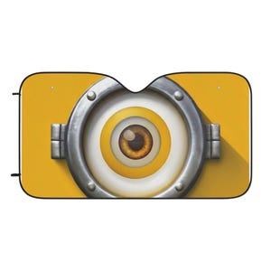 Könnte beinhalten: Gelber Autosonnenschutz mit einem großen, cartoonartigen Augendesign. Das Auge hat eine braune Iris, gelbe und weiße Ringe und ist in einem metallischen, genieteten Rahmen eingefasst. Der Hintergrund ist einfarbig gelb.