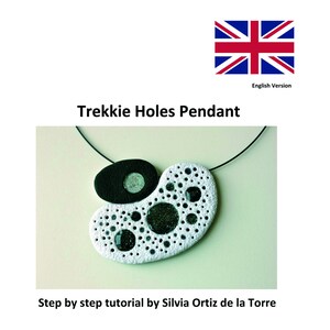 May include: A white pendant with numerous small holes and a black accent piece. The pendant has a black cord and features several dark, glittery embellishments. The text "Trekkie Holes Pendant" is above the image.