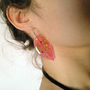 Può includere: Orecchini a forma di foglia rosa con un gancio d'argento e glitter colorati incorporati nella resina.