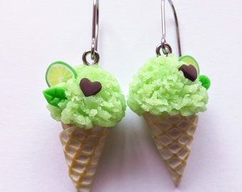 May include: A pair of lime green ice cream cone earrings with a brown heart and a lime slice on top. The earrings are made of polymer clay and have silver hooks.