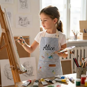 May include: A white and blue striped apron featuring the name Alice embroidered in black script on the chest. The apron includes a front pocket and is decorated with colorful paint splatters, designed for use during artistic painting activities.
