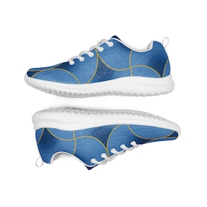 Op de afbeelding: Een paar sportschoenen met een cirkelvormig patroon in blauw en lichtblauw, omlijnd met dunne gouden lijnen. De schoenen hebben witte veters, een witte binnenvoering en dikke witte rubberen zolen met een gestructureerd profiel.