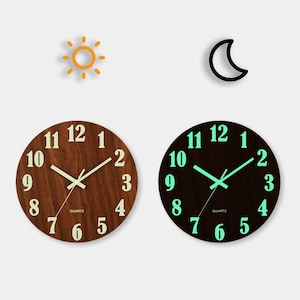 May include: Two round wooden quartz clocks, one with a light wood grain and the other with a black face. The first clock has white numbers and hands, while the second glows green in the dark. A sun and moon graphic are above.