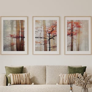 Op de afbeelding: Drie ingelijste kunstdrukken met een mistige bosscène met bomen en rode bladeren. De prints staan boven een beige bank met groene en bedrukte kussens. Een ronde salontafel en vaas staan ervoor.