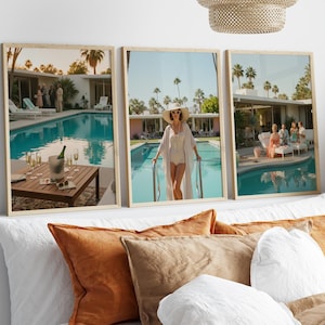 May include: Three framed prints depicting a retro poolside scene with a woman in a white swimsuit and hat, and a table with champagne. The prints are in light wood frames, and the scene is set in a mid-century modern style.