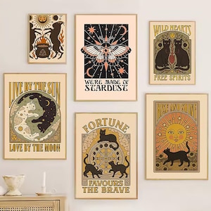 Peut inclure: Plusieurs affiches encadrées avec une esthétique vintage et bohème. Les impressions présentent des thèmes célestes et mystiques, notamment des chats, des papillons de nuit, des soleils, des lunes et du texte comme "We're Made of Stardust" et "Fortune Favors the Brave". La palette de couleurs comprend le beige, le noir et l'or.