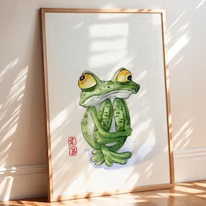 Puede incluir: Ilustración en acuarela de una rana verde con grandes ojos amarillos, abrazando sus piernas. La rana está en un marco de madera, con un sello rojo en la esquina inferior izquierda. La obra de arte está sobre un fondo blanco.