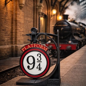 Peut inclure: Un panneau métallique noir pour la plateforme 9 3/4, avec un design circulaire rouge et blanc. Le panneau est devant un train à vapeur dans une gare en briques. Le panneau porte les mots "Platform" et "9 3/4".