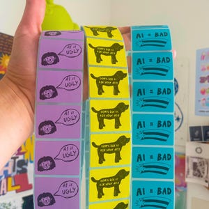 May include: Three vertical strips of rectangular stickers. The purple strip features a person with a speech bubble saying AI is UGLY. The yellow strip shows a dog silhouette with text DON'T ASK AI ASK YOUR DOG. The blue strip displays AI = BAD.