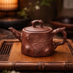 May include: A brown ceramic teapot with a lid and handle, featuring a floral design. The teapot is placed on a wooden tray. The teapot's design resembles a tree trunk, with a spout and handle that mimic branches.