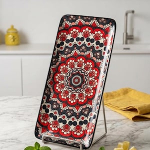 May include: A rectangular ceramic serving tray featuring a vibrant mandala pattern in shades of red, black and white. The tray is displayed upright on a silver metal wire stand, showcasing its intricate geometric design and glossy finish.