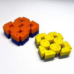 May include: Two sets of colorful geometric building blocks. One set is orange and blue, the other is yellow and gray. The blocks are various shapes, including cylinders, triangles, and squares, and are designed to interlock.