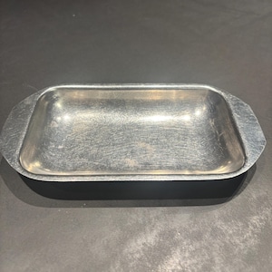 Op de afbeelding: Een rechthoekige, zilverkleurige metalen schaal met afgeronde hoeken en een licht verhoogde rand. De schaal heeft een geborstelde metalen afwerking, met subtiele oppervlakkige krassen. De algemene vorm is een ondiepe rechthoek.