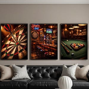 May include: Three framed wall art pieces depicting a dartboard with a dart, a sports bar scene with neon signs, and a pool table with billiard balls. The art pieces are displayed above a black leather sofa.