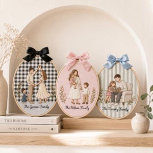 Puede incluir: Tres bastidores de bordado ovalados con retratos familiares personalizados. El bastidor izquierdo tiene un fondo de cuadros blanco y negro con un lazo negro. El central es rosa con un lazo de encaje. El derecho tiene rayas azules y un lazo azul.