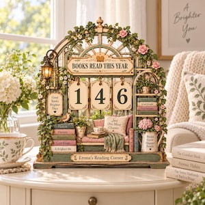 May include: A decorative arched tabletop display titled Emma's Reading Corner, featuring a Books Read This Year counter showing 146, miniature books, a bird, a small lamp, and floral vines. The display includes text reading Good Books Brighter Days, Just One More Chapter, and Books Grow Happier People.