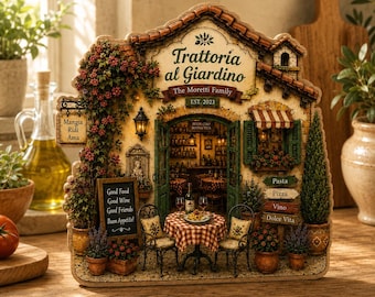 Op de afbeelding: Een decoratief tafelbord in de vorm van een restaurantgevel met het opschrift Trattoria al Giardino The Moretti Family EST. 2023. Het toont een miniatuurscène van een terras met een geblokte tafel, stoelen, potplanten en borden met de tekst Mangia Ridi Ama en Good Food Good Wine Good Friends Buon Appetito.