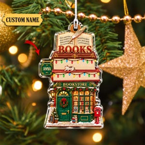 May include: A flat, layered Christmas ornament shaped like a bookstore with a cat on a shelf, a green door with a wreath, and a red mailbox. The top features an open book with the word BOOKS and a quill. A small sign on the side reads ANNA.