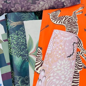 May include: A collection of rolled wallpaper samples featuring various patterns. Designs include floral, botanical, and animal prints, with colors ranging from purple and green to orange and pink. The zebra print is a standout.
