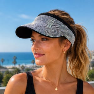 May include: A black visor featuring a wide, curved brim completely covered in small, reflective silver rhinestones. The visor has a solid black fabric band that wraps around the head, providing a secure fit while the sparkling crystals catch light.